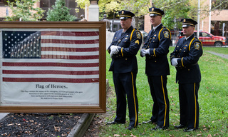 Officers from the Syracuse Police Department stand alongside the Flag of Heroes. The flag is detailed with the names of emergency personnel that gave their lives to save others during the 9/11 terrorist attacks. 