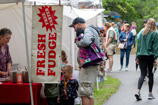 A dad takes his children to get their free sample of fudge. With a variety of options to try, the fudge stand catered to any and all fudge lovers. 